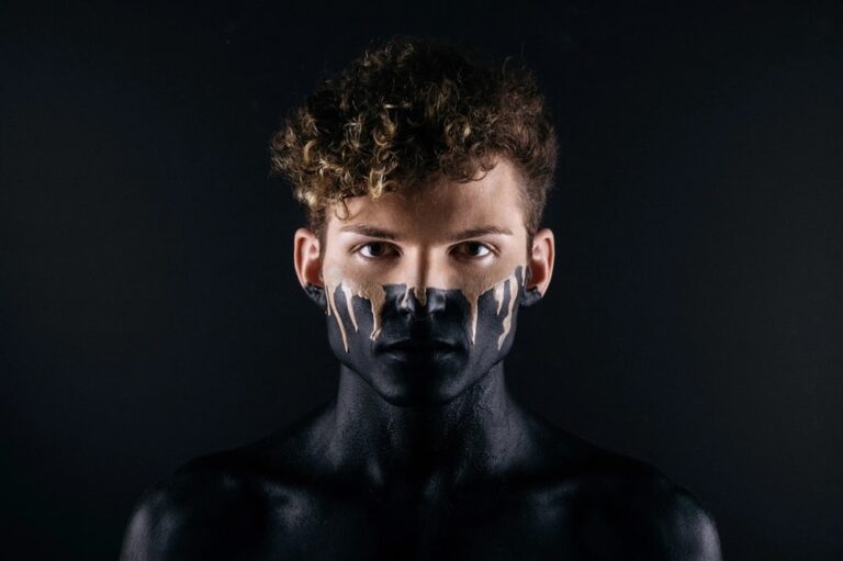 Une photo portrait d'un homme dont la moitié inférieure de son visage et le reste de son corps sont recouverts de peinture noire.